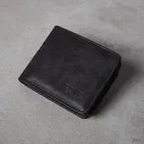 Billetera plegable de eco cuero negro con compartimentos para tarjetas, monedero con cierre, visor y espacios para billetes. Presenta líneas de pespunte decorativas en la parte superior y el logo VCP grabado en relieve.