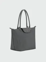 Bolso tote de tamaño mediano, confeccionado en nylon resistente con detalles en cuero. Presenta un diseño minimalista con cierre de cremallera superior, solapa frontal con botón a presión y asas largas para llevar al hombro.