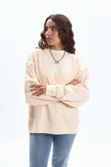 Buzo deportivo color crudo de manga ancha y corte holgado, con cuello redondo y puños y ruedo acanalados.