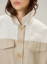 Chaquetas de lino bicolor en tonos blanco y beige, con diseño holgado, cuello alto, cierre frontal de botones, bolsillos con solapa en el pecho y mangas cortas con presilla y botón.