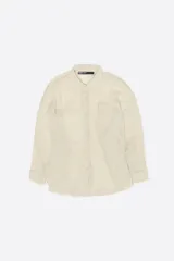 Camisa de manga larga color beige con textura plisada, cuello camisero, cierre frontal de botones, bolsillo en el pecho y bajo redondeado.