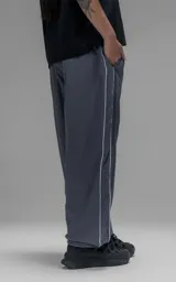 Pantalón deportivo de corte regular confeccionado en microfibra opaca, con cintura elástica y puños ajustables en los tobillos. Presenta vivos laterales a contratono que recorren toda la pierna y un pequeño parche con logo en el frente.