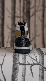 Zapatillas botitas de cuero sintético color blanco con detalles en dorado, negro y glitter negro en el talón.