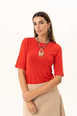 Remera de cuello redondo y manga corta, confeccionada en tejido elástico con un acabado suave y un leve brillo. Presenta un diseño básico con un pequeño isotipo bordado en la espalda.