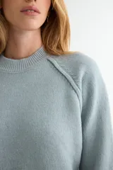 Buzo de tejido de punto en color rosado, con cuello redondo, mangas largas y puños acanalados. Presenta un diseño de tejido texturizado en la parte inferior y en los puños.