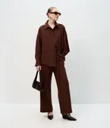 Camisa de corte oversized con estilo sastre, confeccionada en tejido plano. Presenta cuello clásico, cierre frontal con botones, mangas largas con puños anchos y sisas desplazadas.