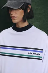 Remera de manga larga blanca con cuello alto en color azul. Presenta franjas horizontales de colores en el pecho y el logo de la marca estampado.