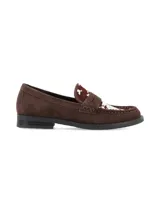 Zapato tipo mocasín de gamuza color marrón, con detalle de pelo sintético con estampado de vaca en la parte superior y suela plana de goma.
