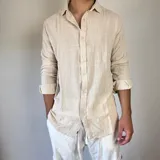 Camisa de lino con corte oversize, cuello clásico y cierre frontal con botones. Presenta mangas largas con puños arremangados y una textura rústica característica del tejido.