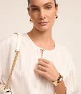 Blusa blanca de chiffon con cuello redondo y abertura en forma de gota en el frente. Tiene mangas 3/4 y rayas de hilo teñido metalizado.