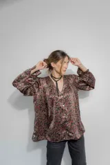 Camisa de seda con estampado floral en tonos bordó, marrón y negro. Presenta un corte amplio, escote en V con cierre frontal de botones, mangas largas abullonadas y frunces en hombros y espalda.