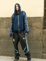 Hoodie con cierre frontal, tejido en algodón con diseño reversible. Presenta detalles de roturas intencionales en puños, ruedo y costuras, con estampado gráfico en mangas y capucha.