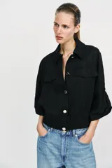 Blusa negra de cuello solapa y manga corta, con bolsillos con solapa en el pecho, bajo elástico y cierre frontal con botones.