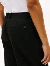 Pantalón negro de corte amplio, tobillero y talle bajo. Confeccionado en tejido antiarrugas de mezcla de viscosa elástica. Presenta cierre de cremallera con enganche oculto, raya marcada en la parte delantera y trasera, y dos bolsillos traseros de ojal.