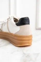 Zapatillas bajas de cuero color blanco y beige, con suela gruesa marrón y cordones blancos.