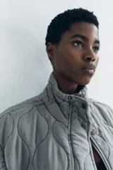 Chaleco gris acolchado con cuello alto, cierre frontal con cremallera metálica, bolsillos de plastrón en delantero y bajo ajustable con cordones.