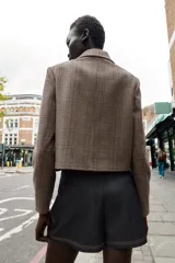 Blazer corto de corte estructurado con cuello solapa, manga larga y hombreras. Presenta cierre frontal con botones metálicos y dos bolsillos delanteros de plastrón con solapa. Diseño con estampado de cuadros tipo príncipe de gales.