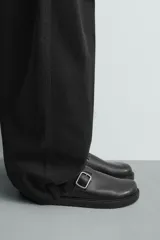 Zueco destalonado de cuero negro con suela de plataforma plana y detalle de hebilla metálica plateada en el empeine.