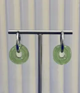Aros tipo argolla con dije colgante en forma de dona de vidrio color verde traslúcido. La estructura de la argolla es de plata 925.