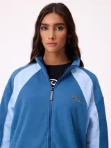 Campera de polar marca Rusty, color azul con paneles laterales en celeste claro. Presenta cierre frontal completo, cuello alto y logo de la marca bordado en el pecho.