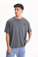 Remera oversize gris de manga corta con efecto lavado acid wash y estampa pequeña en el pecho con la palabra 'START' dentro de un recuadro amarillo.
