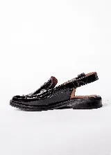 Mocasines tipo slingback de cuero charolado negro, con taco bajo de 1.5 cm y tira frontal decorada con tachas metálicas. Presenta una tira ajustable con hebilla en el talón.