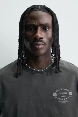 Camiseta de corte relajado con cuello redondo y mangas cortas. Presenta un efecto lavado que le otorga una apariencia única y estampados a contraste en el frente.