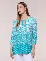 Blusa azul y blanca con estampado floral y geométrico, de calce suelto, con escote redondo, abertura tipo keyhole en el pecho, mangas tres cuartos y ruedo amplio con silueta evasé.