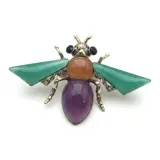 Broche con forma de mosca realizado en metal dorado envejecido, con alas de resina verde, cuerpo central de resina naranja, abdomen de resina violeta y ojos de cristal negro.
