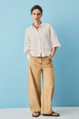 Camisa blanca de lino, con mangas anchas a tres cuartos, cuello clásico, cierre frontal con botones y detalles de calados verticales en la parte central y en los puños.