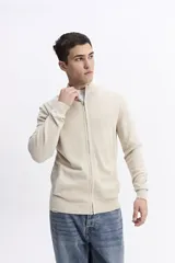 Campera tejida de algodón en color beige, con cierre frontal completo, cuello levemente elevado y puños y ruedo acanalados. Presenta un pequeño logo bordado en el pecho.