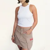 Minifalda cargo color beige, con múltiples bolsillos frontales y traseros. Presenta un pequeño logo bordado en rojo en uno de los bolsillos laterales.