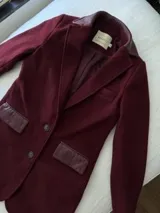 Tapado de lana color bordó con solapas y detalles en los bolsillos de cuero. Presenta cierre frontal con botones y diseño de líneas clásicas.