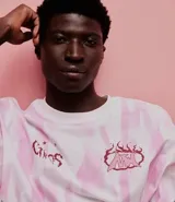 Remera oversized de algodón con teñido tie-dye en blanco y rosa. Presenta un cuello redondo y un estampado frontal con la palabra "Chaos" y un diseño de llamas en color rosado.
