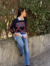 Sweater de tejido de punto con diseño geométrico en tonos azul marino, azul y detalles en rojo. Presenta cuello redondo y mangas largas con bordados lineales.