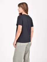 Remera gris oscuro de manga corta con cuello redondo. Presenta un estampado frontal con dos figuras femeninas estilizadas, una vestida de rosa con una estrella blanca y la otra con un look negro y rojo.