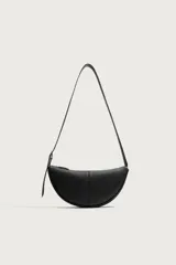 Bolso de hombro pequeño color negro con acabado liso, diseño semilunar y costura central. Cuenta con compartimento principal con cierre de cremallera, bolsillo interior con cierre y asa de hombro ajustable con hebilla.