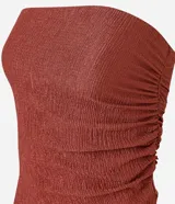 Top tipo bandeau sin breteles, color rojo oscuro o terracota, con textura plisada o arrugada y un detalle de caída asimétrica en un lateral.