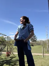 Camisa tipo vestido a rayas celestes, rojas y blancas, con cuello alto fruncido, mangas cortas abullonadas con puños elásticos y cierre frontal de botones.