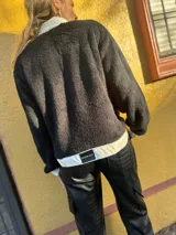 Campera de corderito negra con cuello, solapa, puños y bolsillos de cuero sintético color crema.