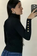 Polera de hilo blanca de cuello alto y manga larga, con detalle de botones dorados en los puños. Tejido de punto acanalado ajustado al cuerpo.
