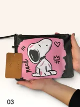 Sobre de cuero marrón con diseño pintado a mano que presenta al personaje Snoopy sobre un fondo rosado y la palabra 'heal'. Cuenta con cierre superior y etiqueta de cuero colgante.