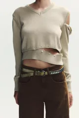 Jersey de punto con cuello en V y manga larga. Presenta un diseño versátil con detalles de acabados desmontables mediante botones en la parte inferior y en los hombros.