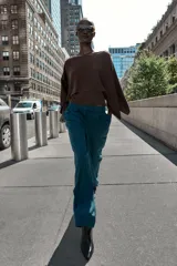 Pantalón de vestir marrón oscuro, tiro alto, con pernera ancha y pinzas frontales. Presenta un bolsillo con tapeta en la parte superior delantera.