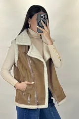 Chaleco tipo gamulán color marrón con interior y bordes de corderito sintético color crema. Presenta cierre frontal y bolsillos laterales con cremalleras metálicas, además de detalles de tiras de cuero sintético.