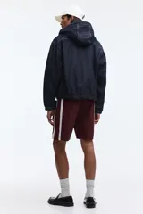 Short deportivo de nylon color bordó, con franjas laterales blancas, cintura elástica con cordón de ajuste blanco y bolsillos laterales.
