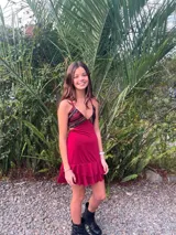 Vestido corto de tela metalizada en tono fucsia con reflejos dorados, con escote en V, diseño de top con triángulos, aberturas laterales en la cintura y doble volado irregular en el ruedo.