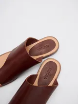 Sandalias planas de cuero color marrón, con diseño minimalista que sujeta el dedo pulgar y deja el empeine al descubierto.