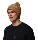 Gorro de punto tejido color marrón tostado con textura acanalada, forro micropolar interno, pompón superior y parche con el logo de la marca en el lateral.