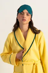 Bata clásica amarilla con textura capitoné y ribete verde en cuello, solapa, puños y cinturón.